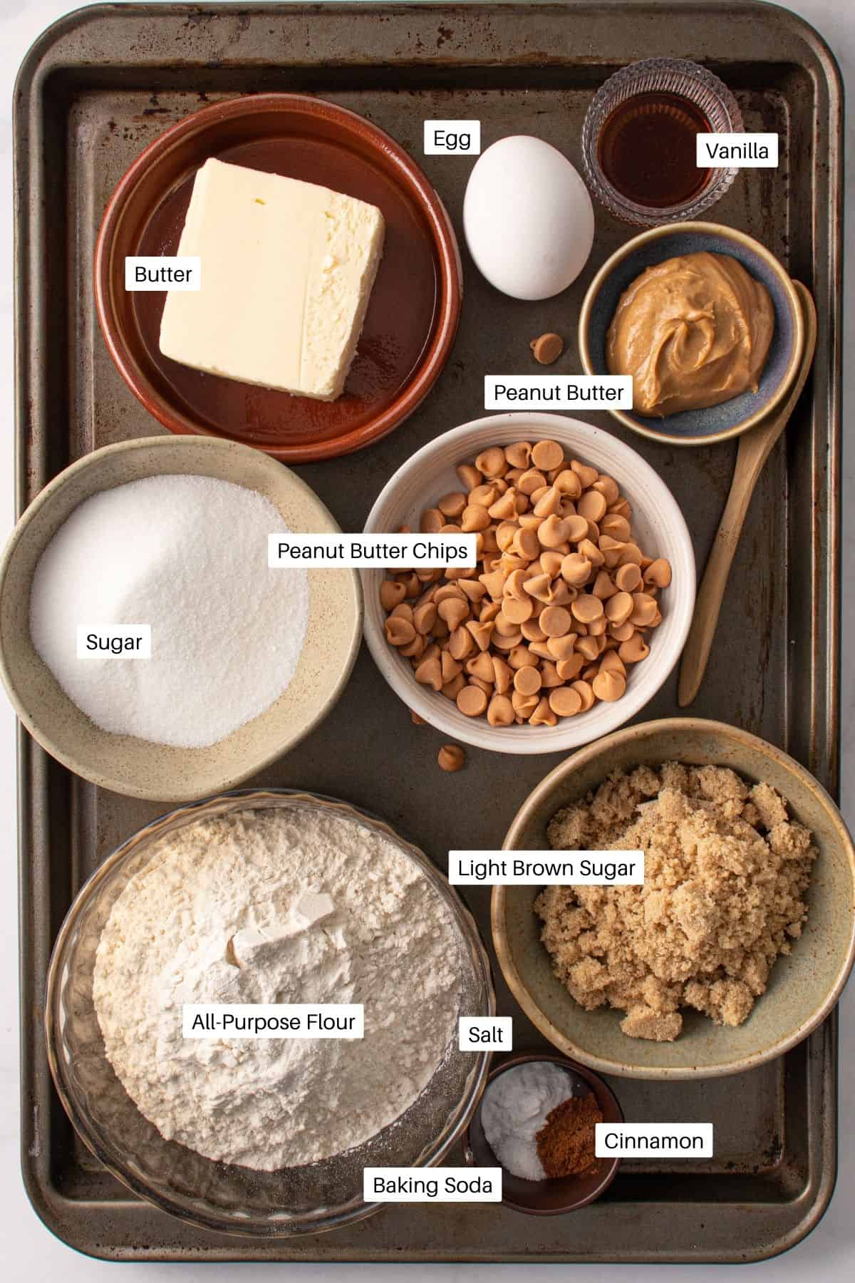 Butter, egg, vanilla, peanut butter, peanut butter chips, sugar, brown sugar, flour, salt, cinnamon and baking soda on a baking dish.