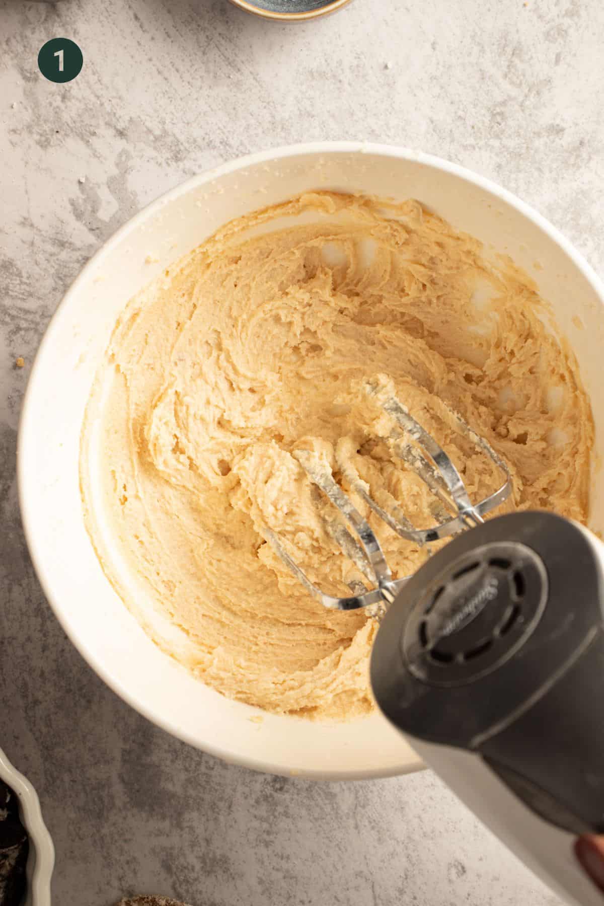 Butter and sugar being creamed in a bowl with a hand mixer. 