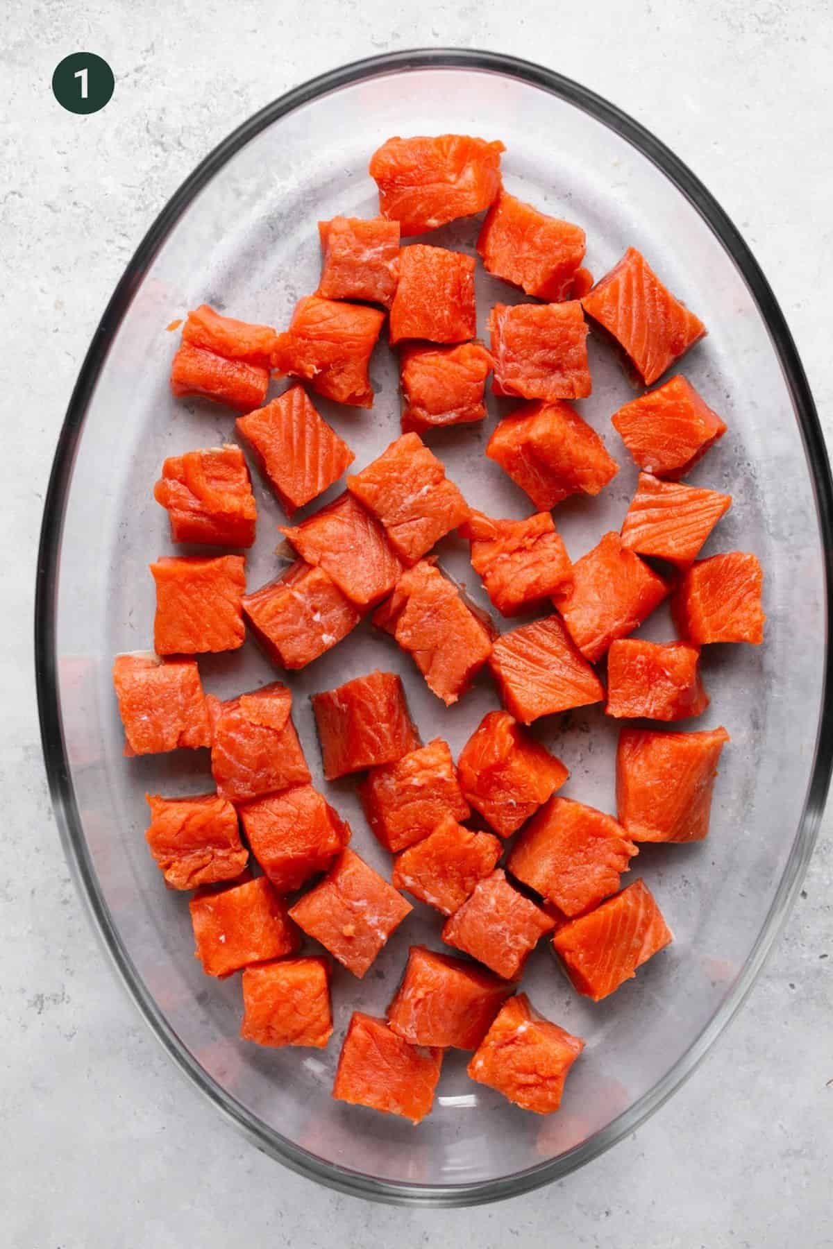 Raw wild caught salmon filet chopped into one inch squares on a glass plate.