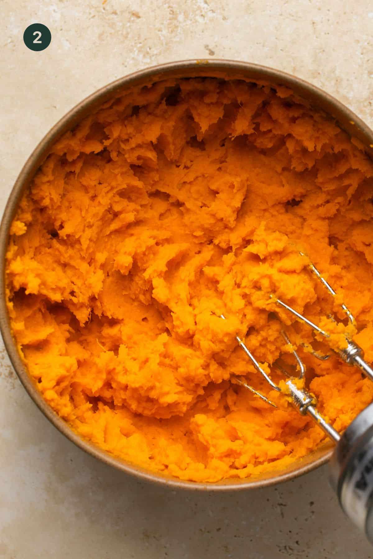 Mashed sweet potatoes using a hand mixer in a bowl.