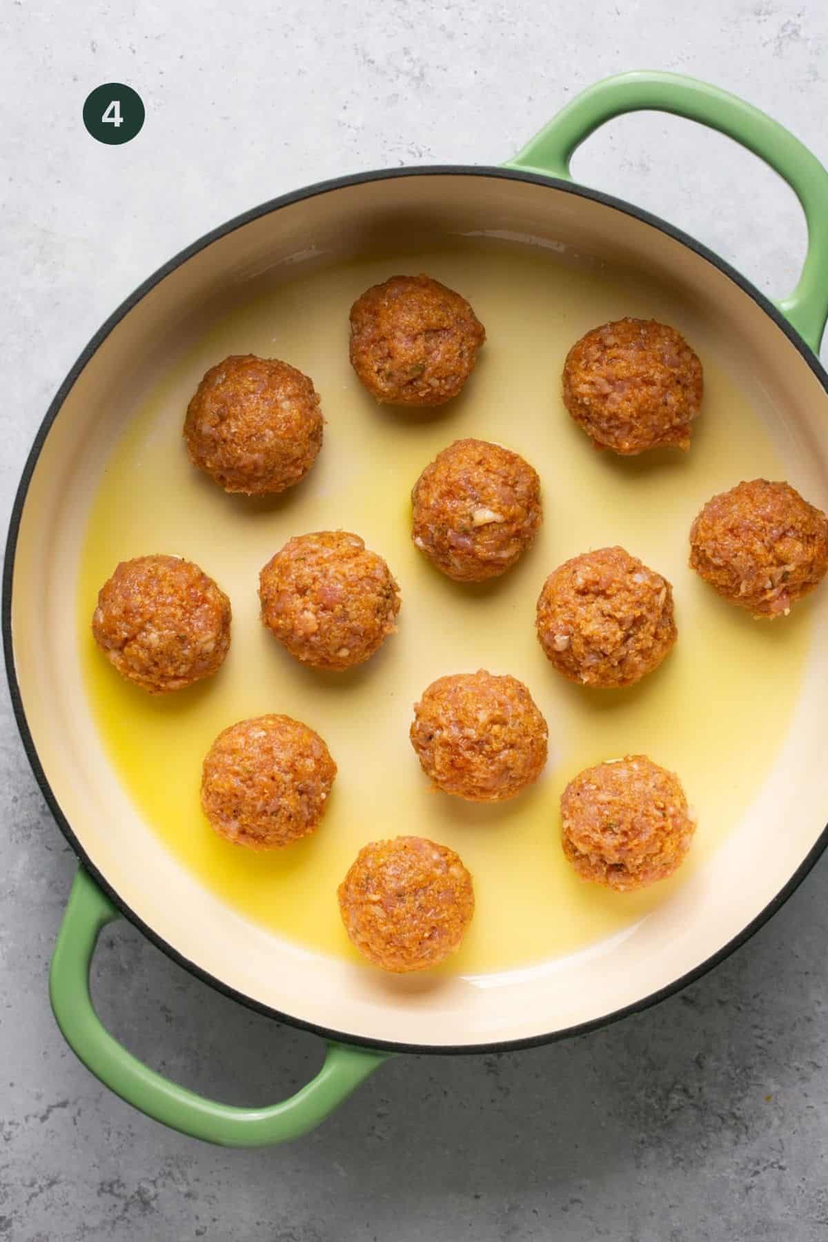 Olive oil in a pan with raw meatballs to cook. 