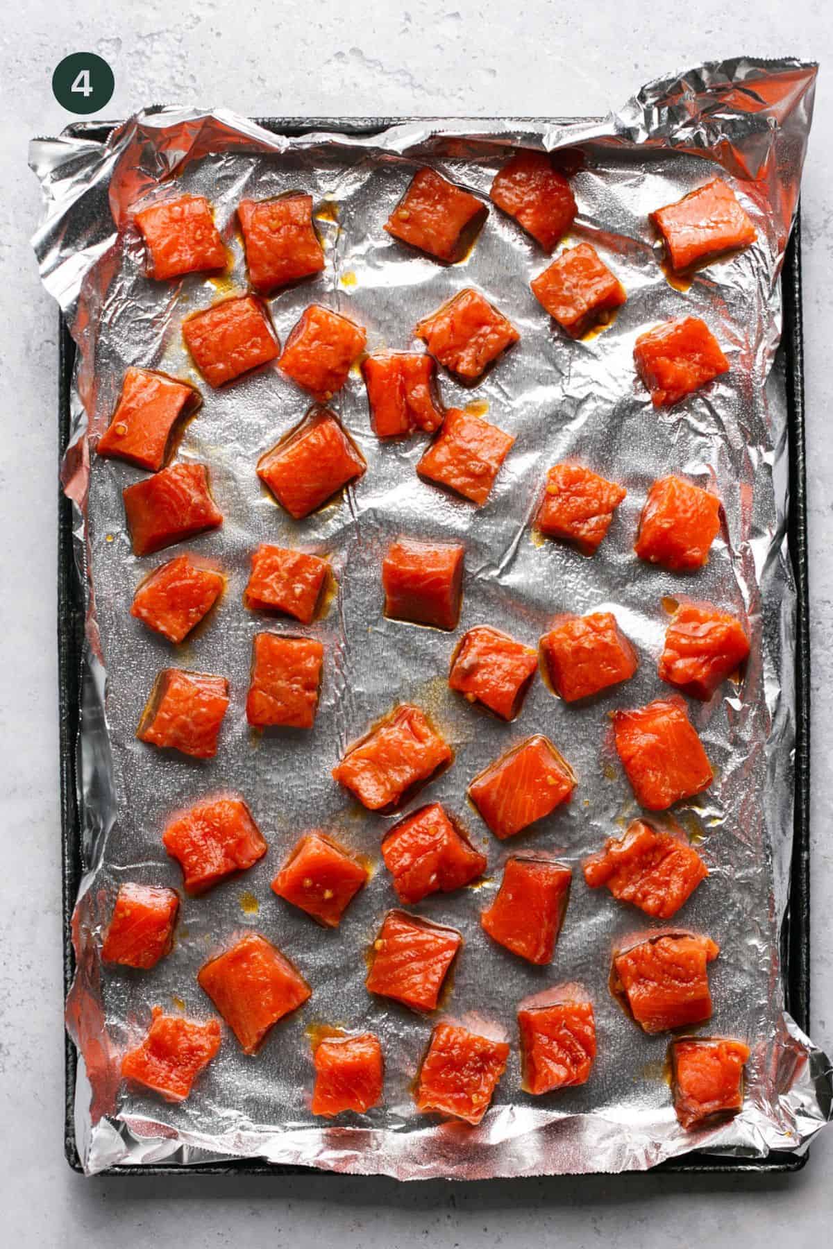 Cubed marinated raw salmon on foil lined baking sheet. 