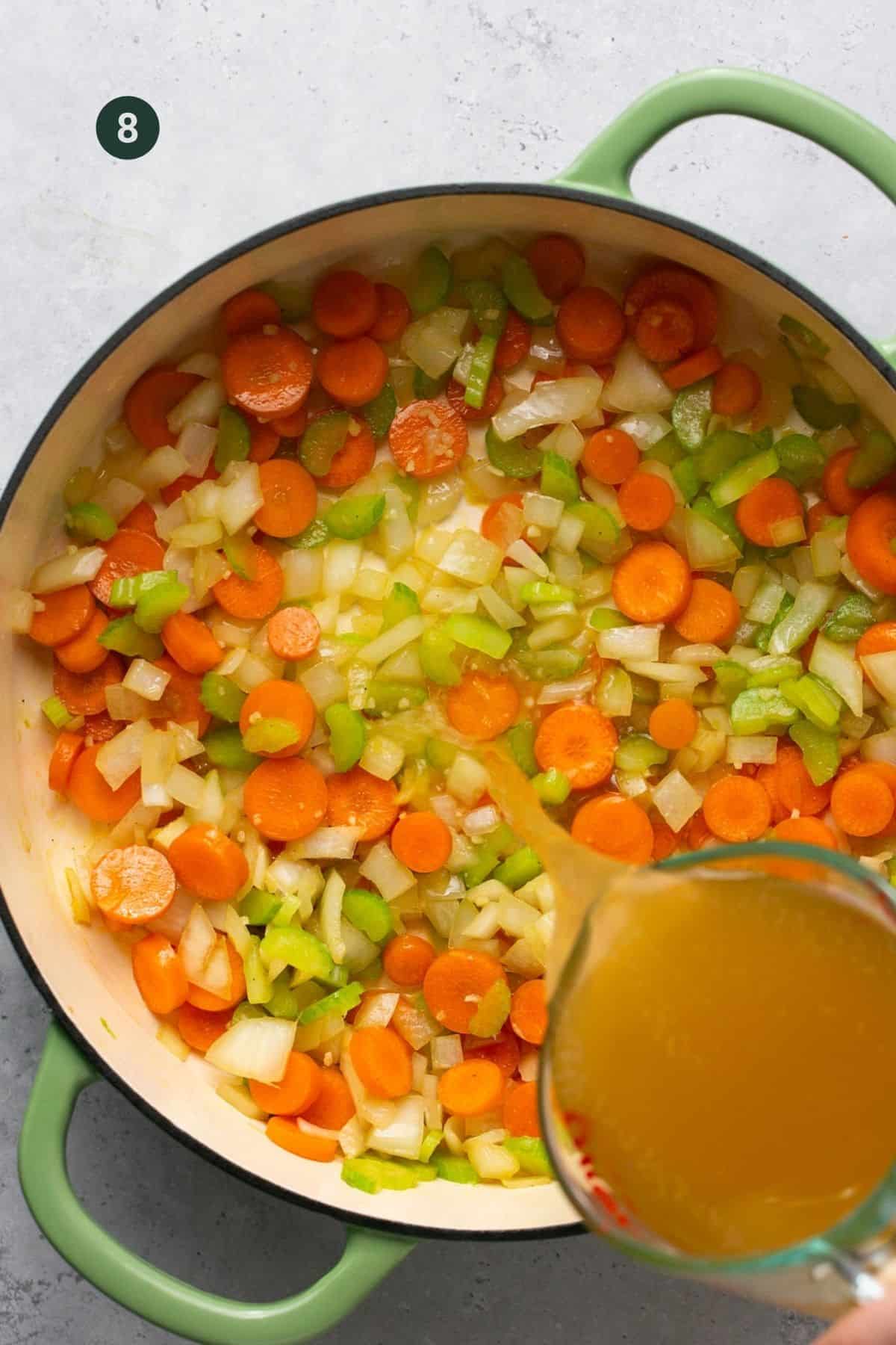 Beef broth being added to a pot of vegetables.