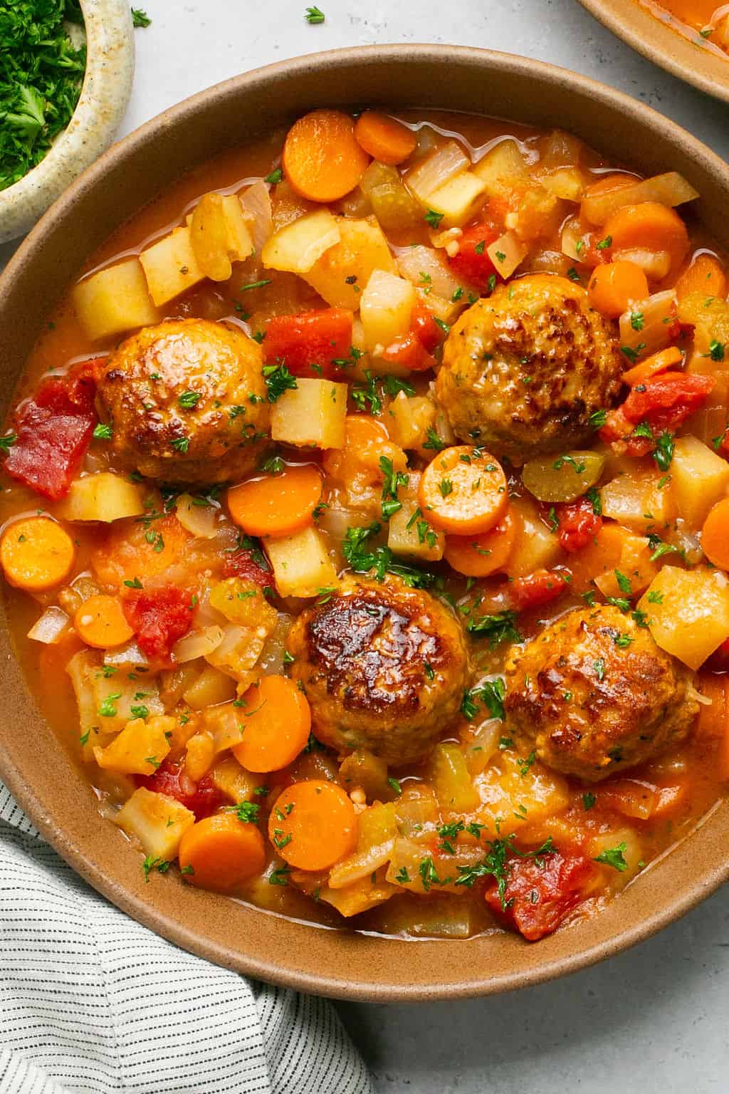 Plated stew in a bowl with chopped potatoes, carrots and full meatballs with parsley garnish. 