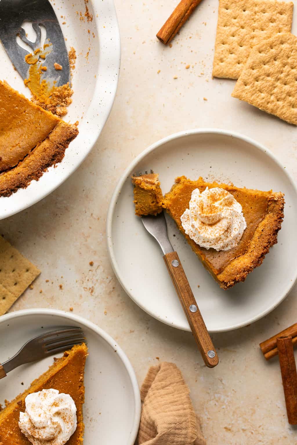 Two plated slices of pumpkin pie with whipped cream and cinnamon on top and one with a bite taken out of it.