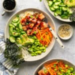 Three assembled teriyaki salmon bowls over riced cauliflower with extra sauce and green onions for topping.
