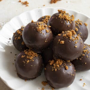 Chocolate covered truffles on a plate with biscoff cookie crumbs on top.