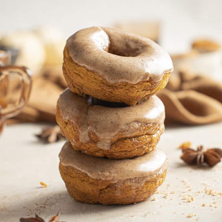 Three glazed pumpkin donuts stacked on one another.