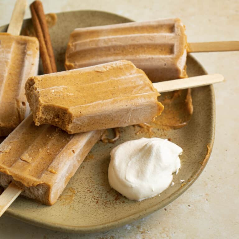 Pumpkin popsicles on a plate with a bite taken out of one.