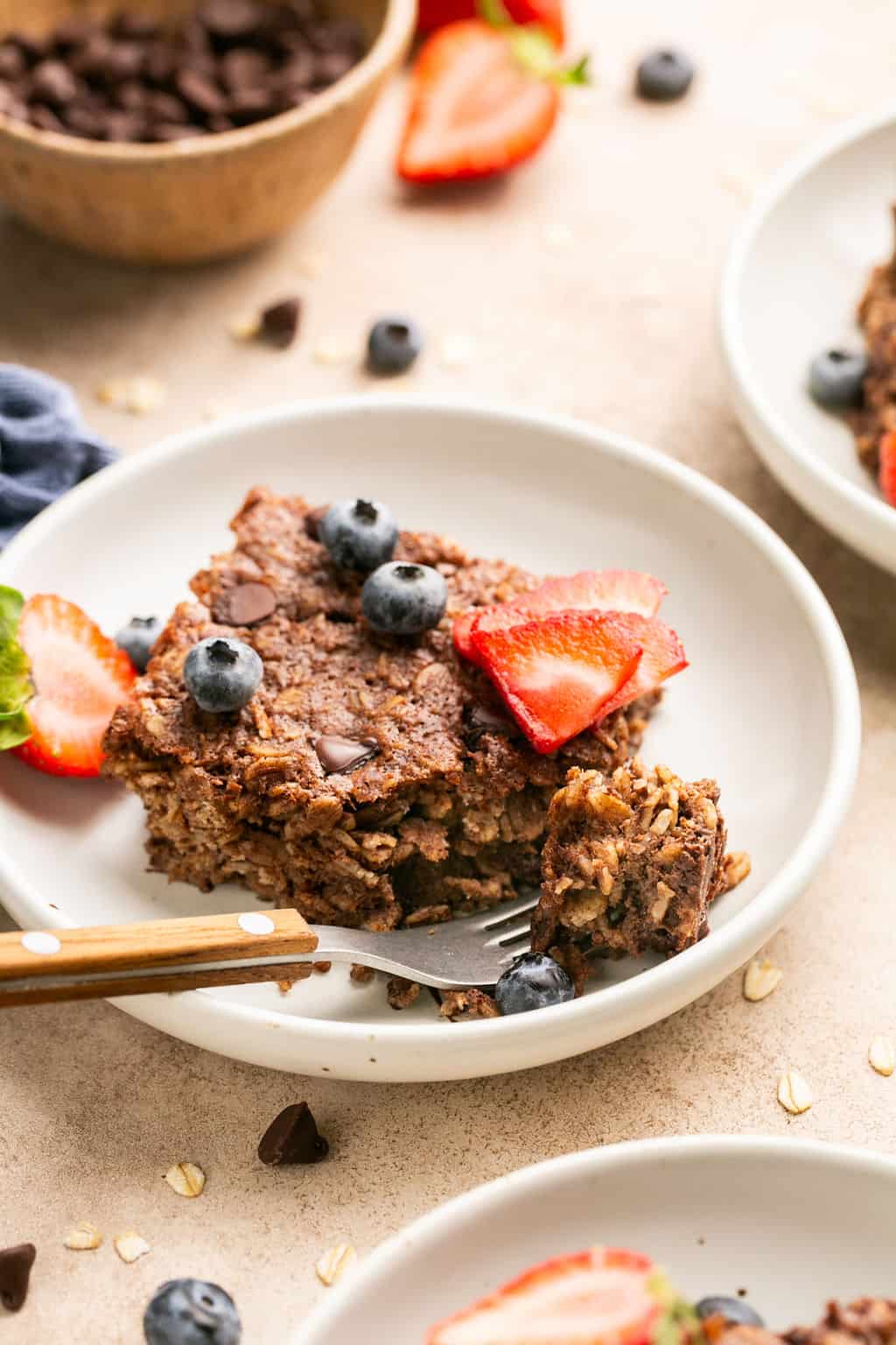 Baked oatmeal square on a dish with sliced strawberries and blueberries. 
