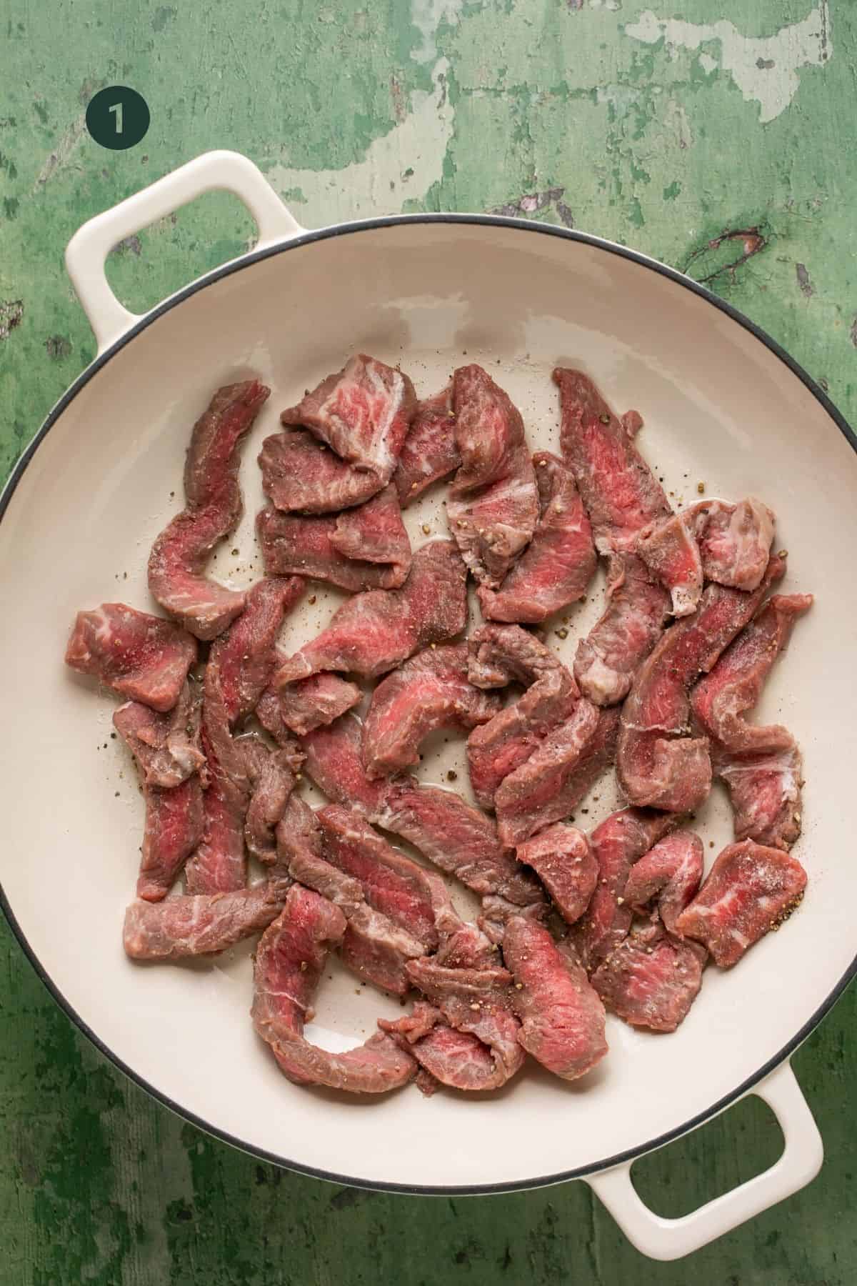 Raw beef sliced in a pan to sear. 