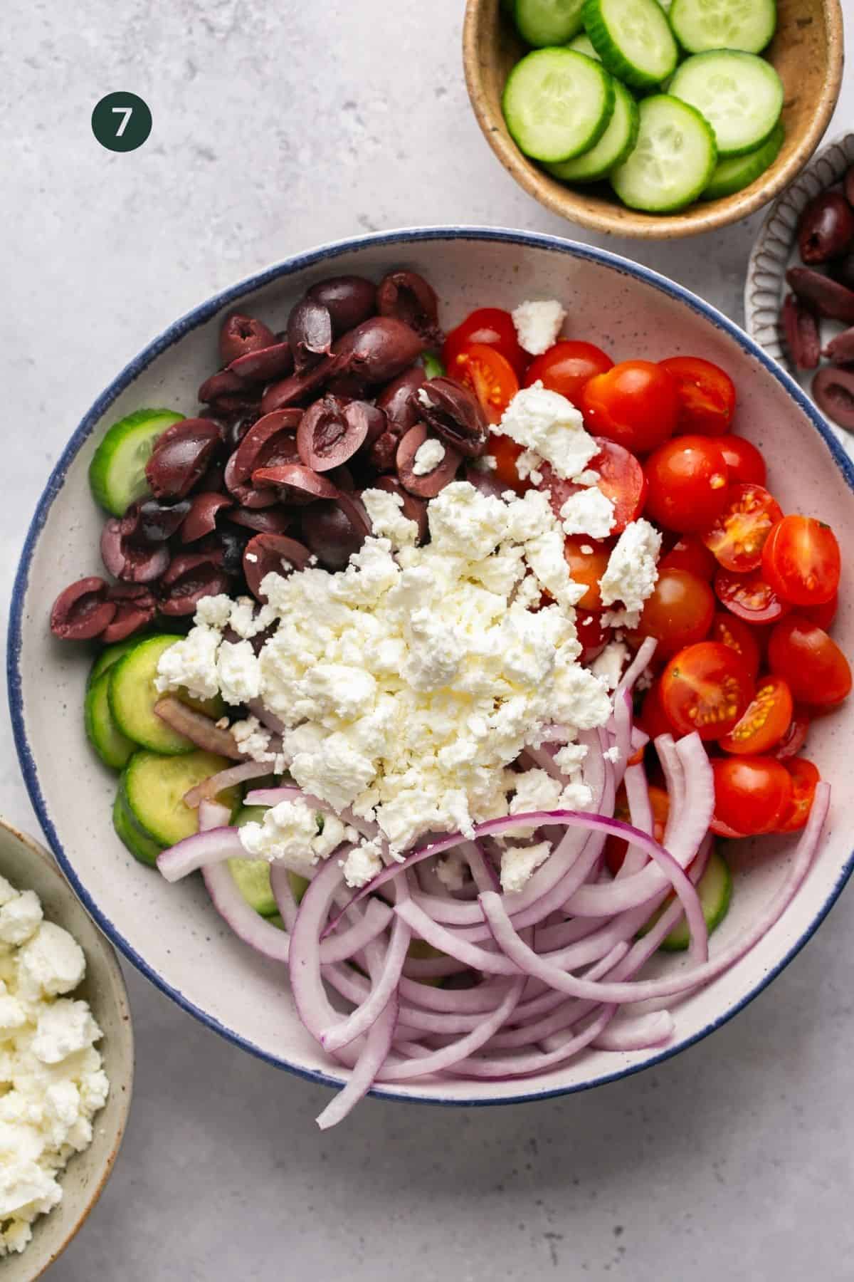 Tomatoes, red onion, cucumber, kalamata olives and feta in a bowl. 