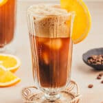 Coffee mocktail with orange slice as garnish surrounded by orange slices and coffee beans.