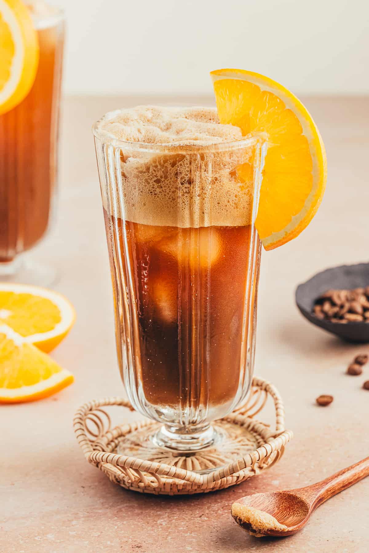 Coffee mocktail with orange slice as garnish surrounded by orange slices and coffee beans. 