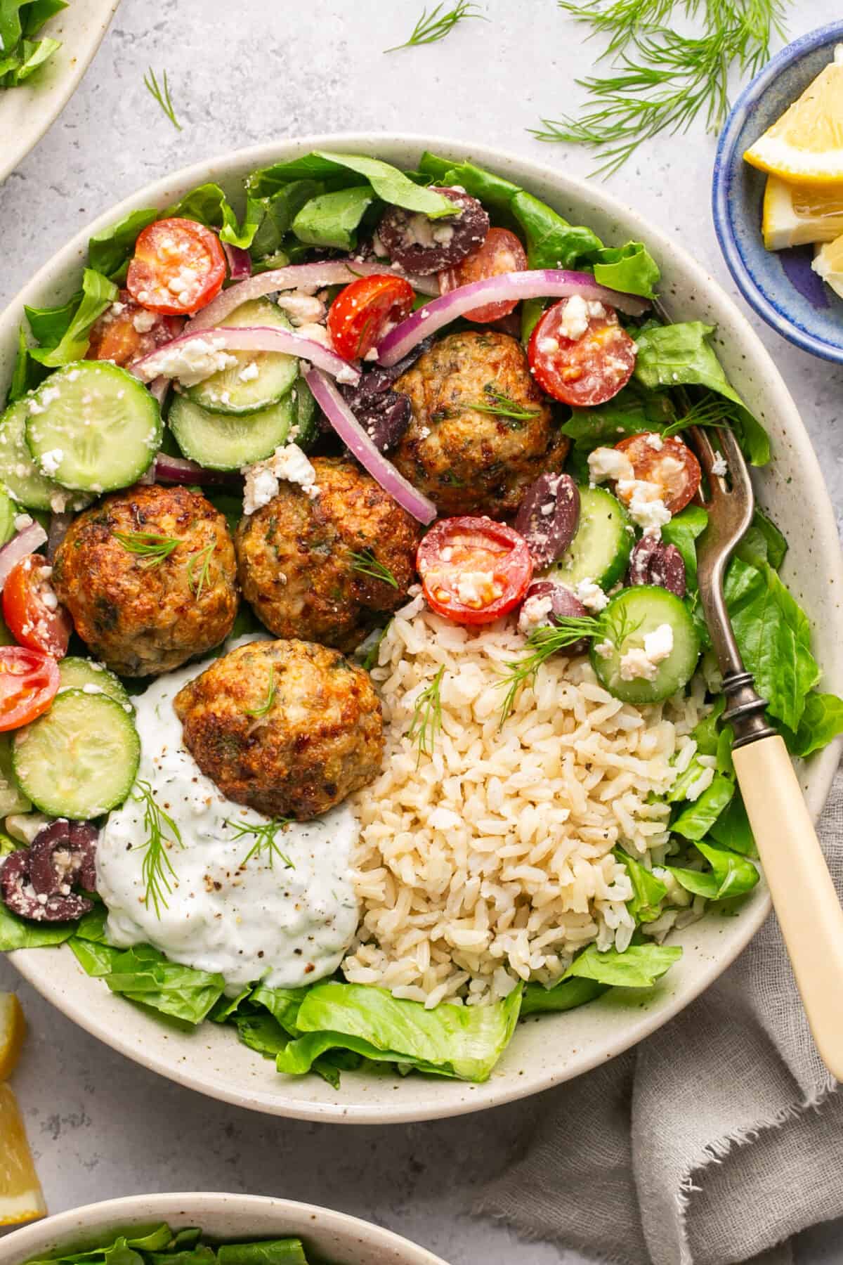 Bed of lettuce topped with brown rice, greek salad mixture, homemade tzatziki and meatballs.