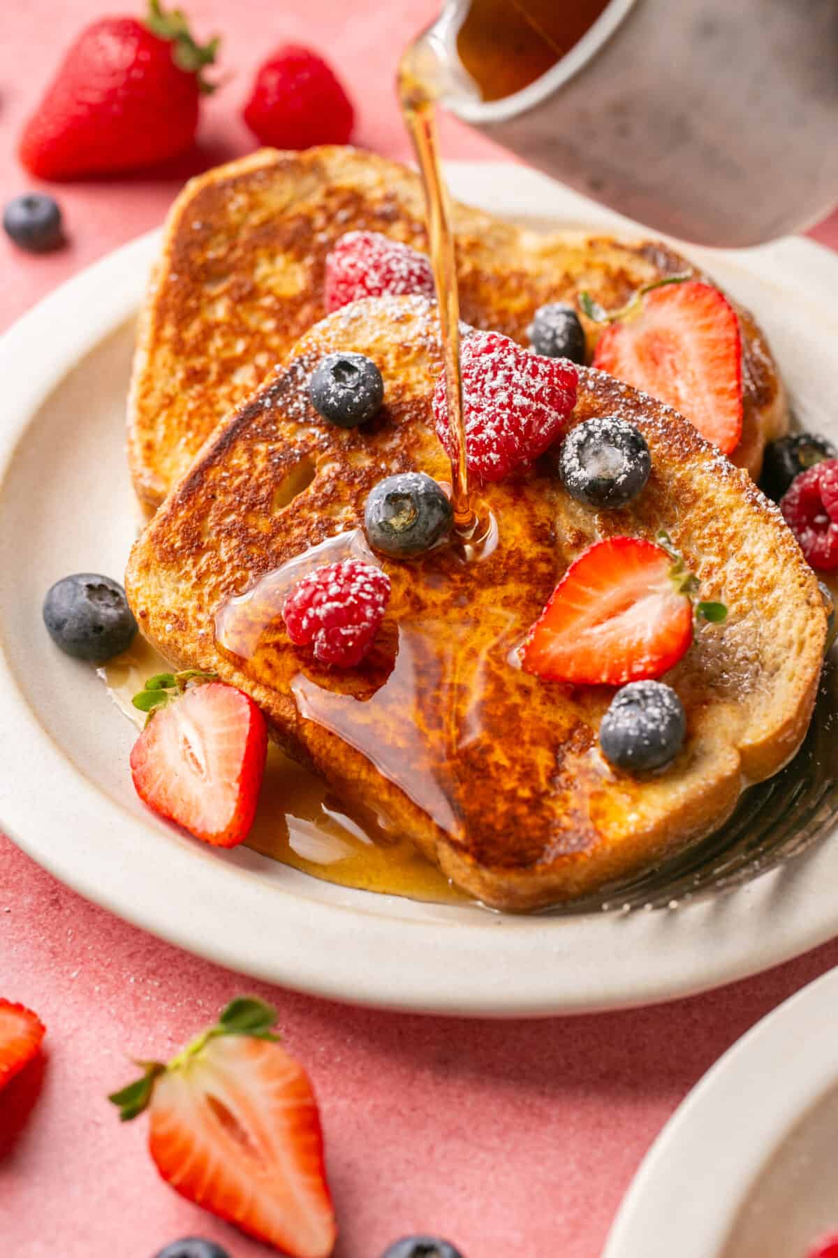 Berries and powdered sugar on browned french toast and syrup being poured on top. 