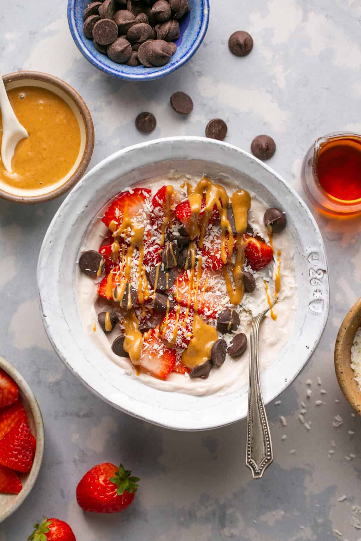 Yogurt bowl with sliced strawberries, chocolate chips and peanut butter drizzled on top. 