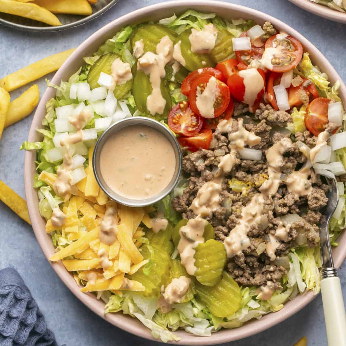 Burger salad bowl with sauce on top and on the side.
