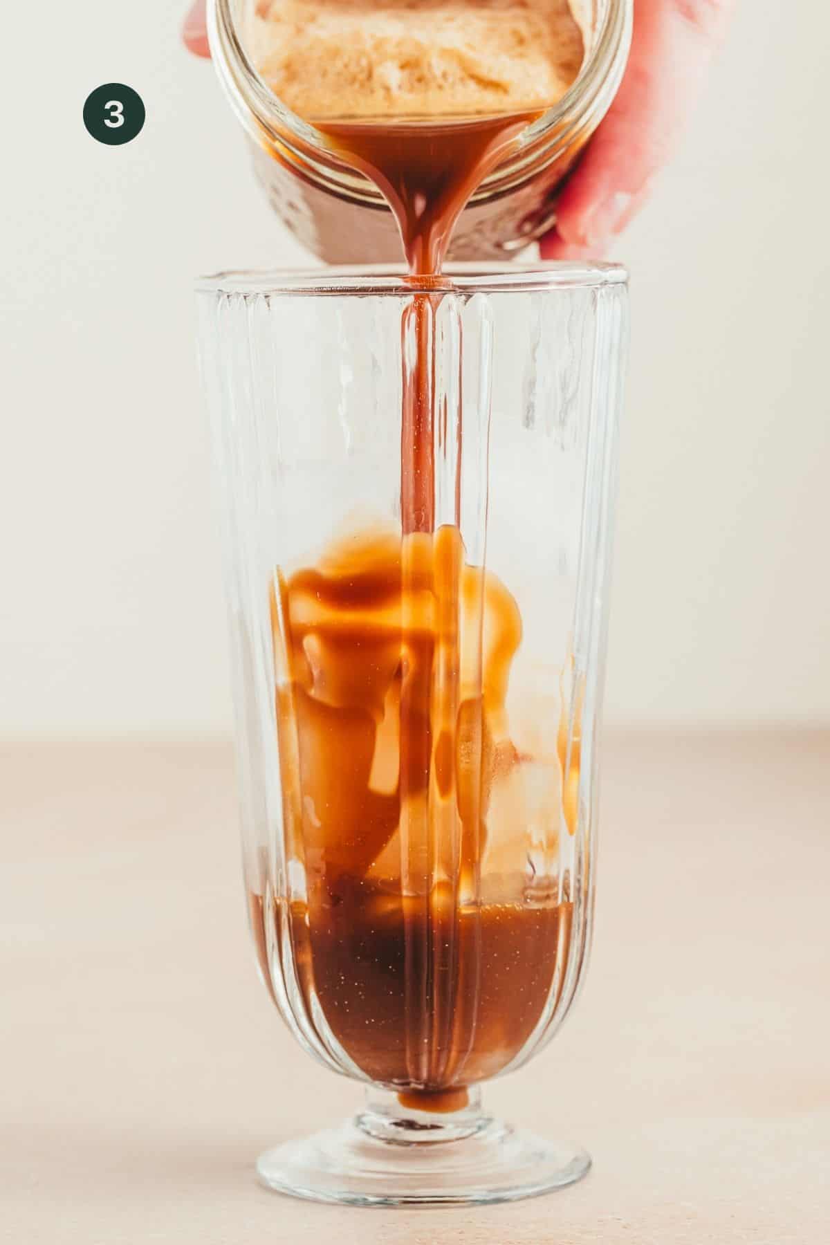 Pouring the shaken coffee mixture into a tall glass with ice. 