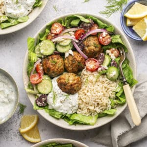 Mediterranean chicken meatballs in a bowl of lettuce and rice with homemade tzatziki and greek salad.
