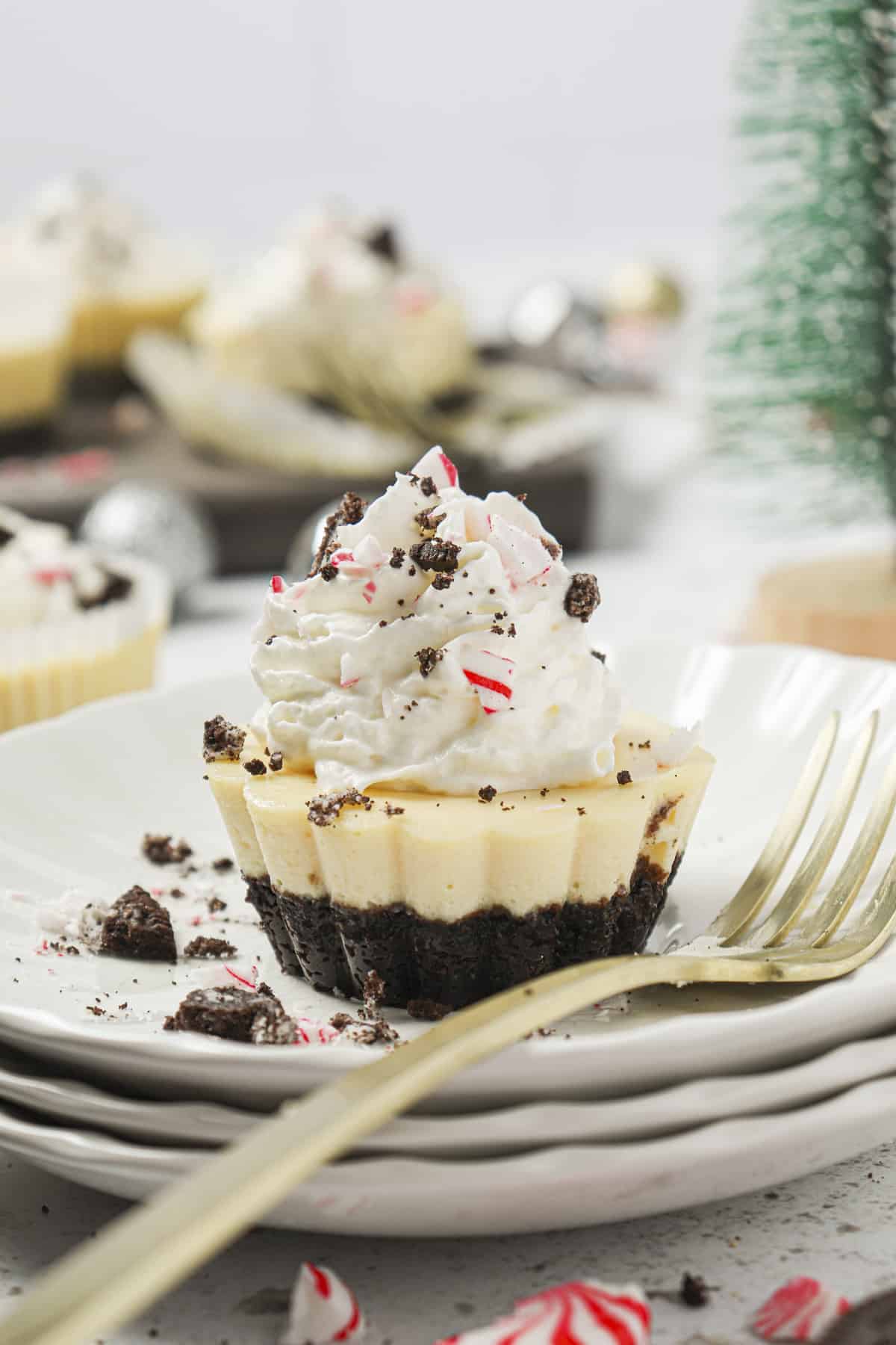 Oreo peppermint cheesecake on a plate with whipped cream, crushed peppermints and Oreos on top.