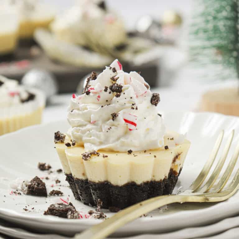 Oreo peppermint cheesecake on a plate with whipped cream, crushed peppermints and Oreos on top.