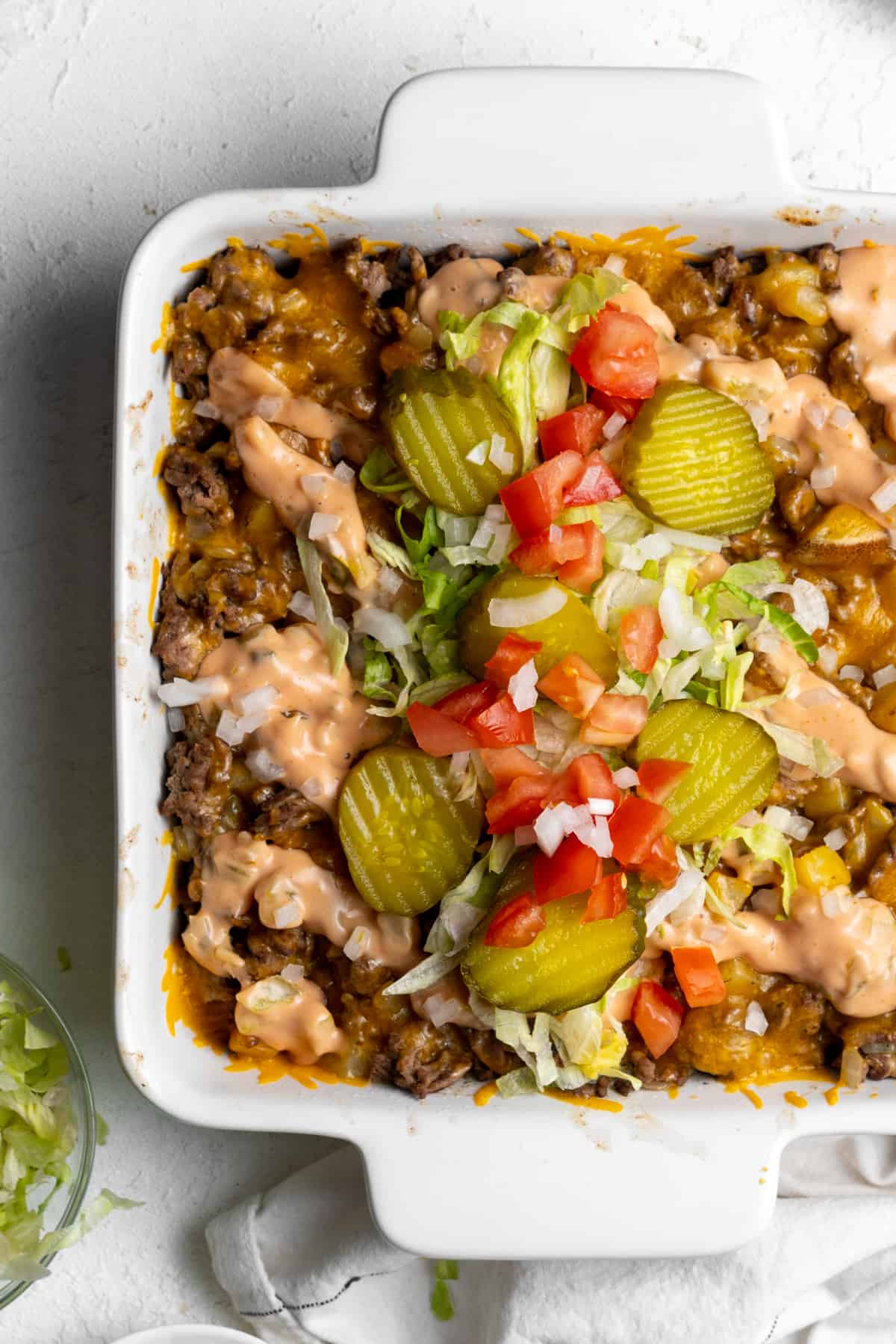 Big Mac Casserole in a casserole dish with lettuce, pickles, onions and tomatoes on top. 