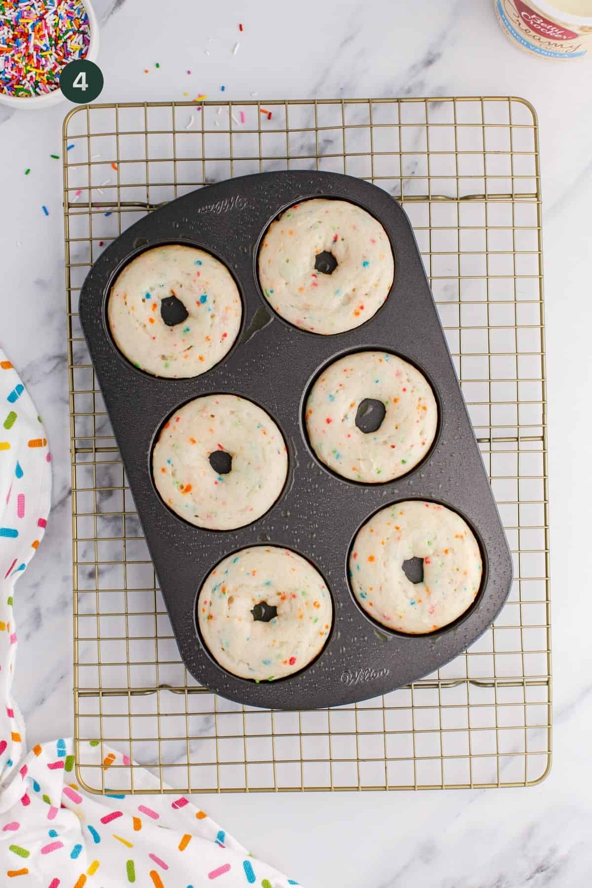 Six baked donuts in a donut pan on a wire rack.