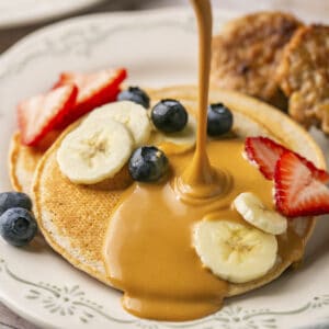 Peanut butter sauce being poured on top of pancakes.
