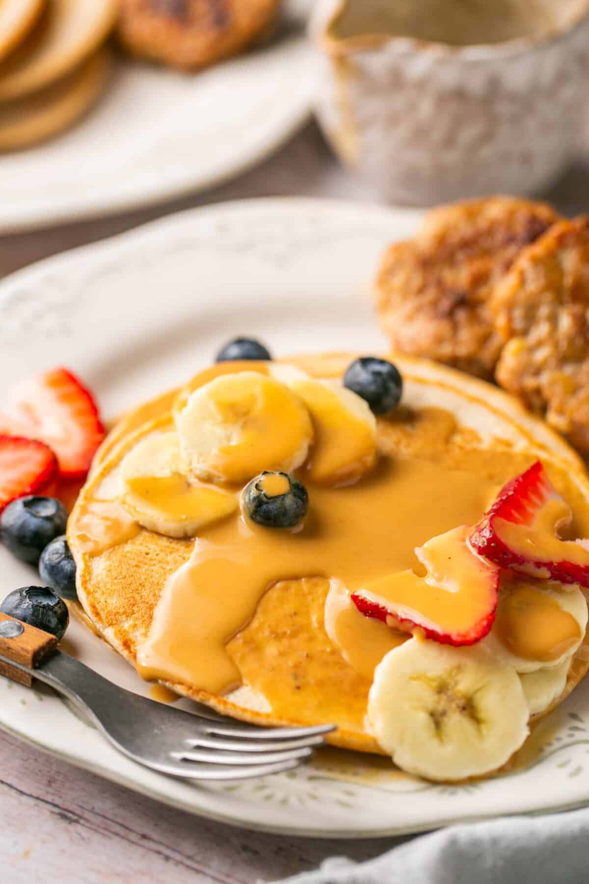 Pancakes covered in the peanut butter sauce with berries and sliced bananas on top. 