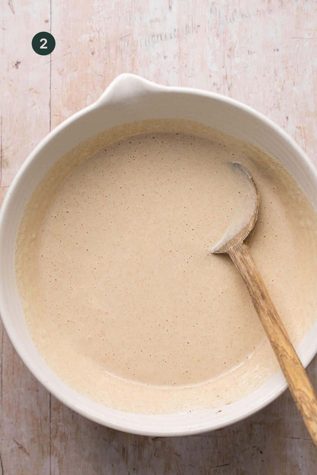 Fully combined pancake batter in a mixing bowl with a wooden spoon. 