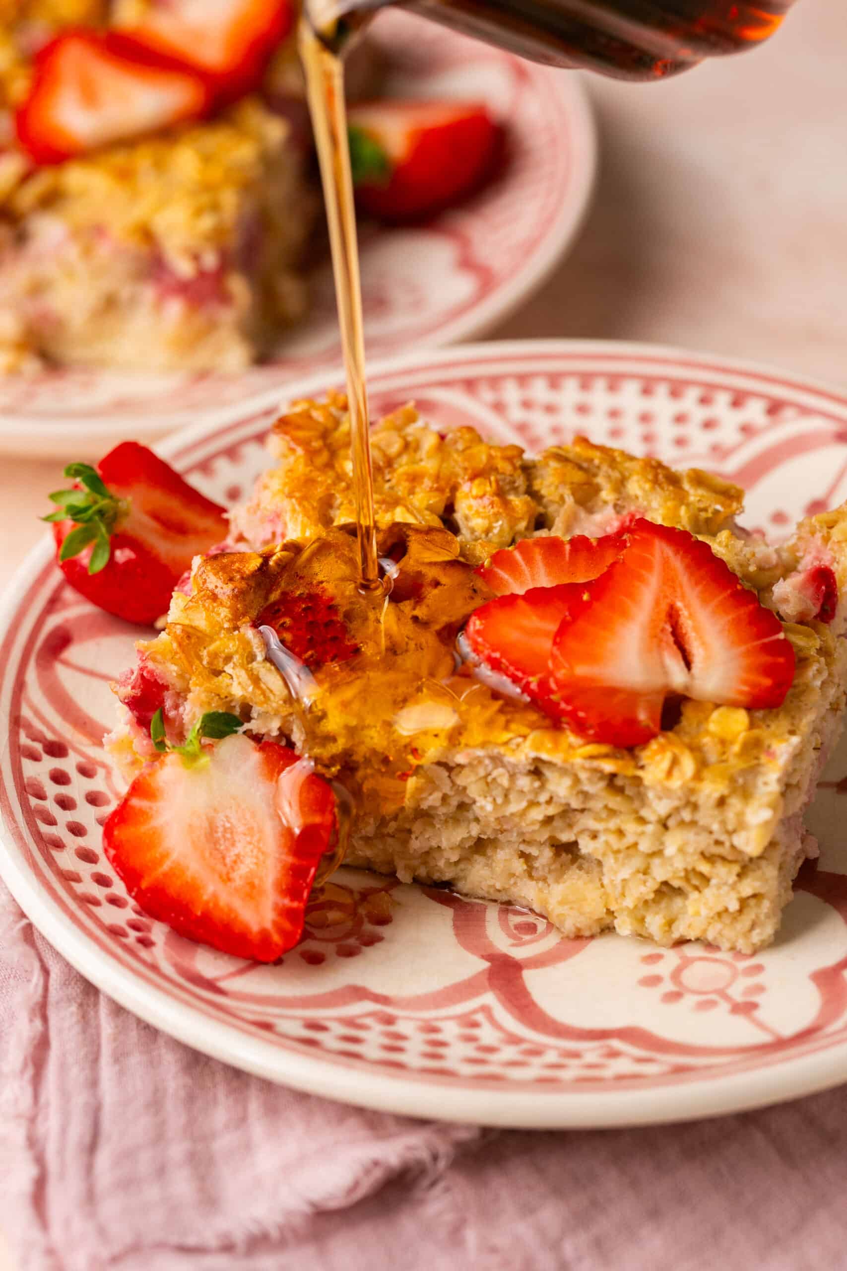 Slice of baked oats with strawberries on top and maple syrup being poured on top.