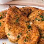 4 cooked and browned breaded chicken cutlets on a plate.