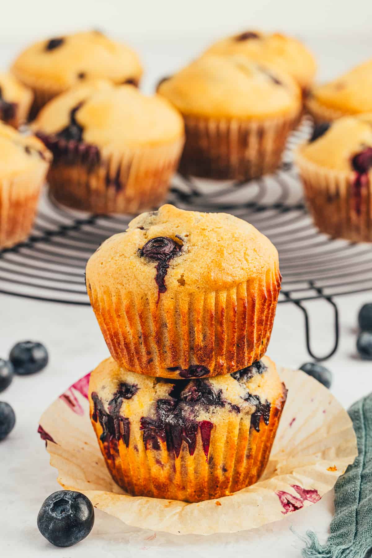 Two stacked blueberry muffins with muffins cooling behind them. 