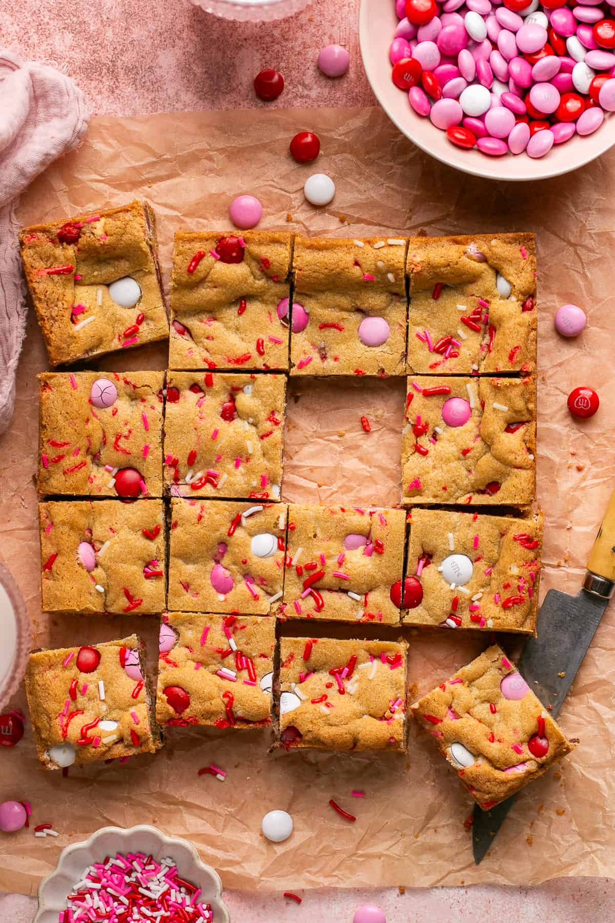 Over head of the freshly baked and cut into 12 squares cookie bars with M&M's and sprinkles scattered around.