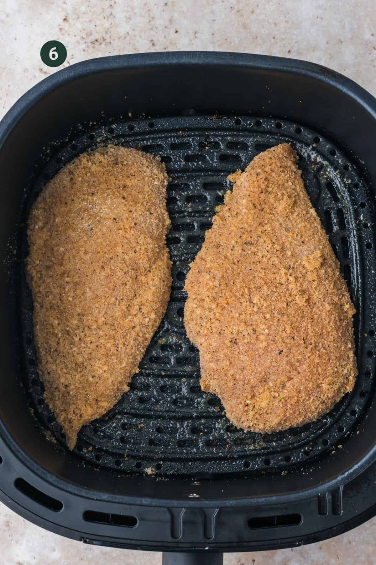 Fully coated chicken breast in the air fryer basket to cook.