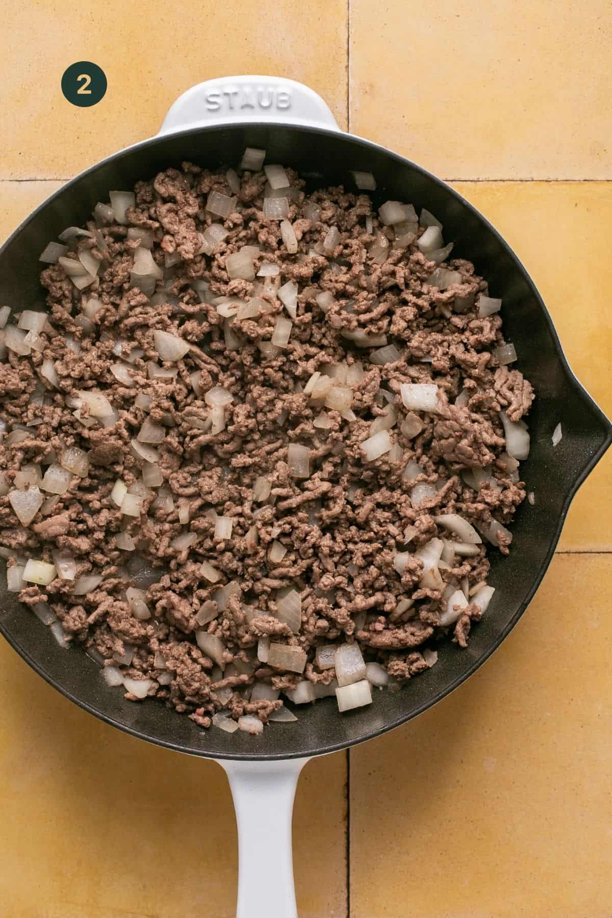 Browned and cooked beef and onions in a pan.