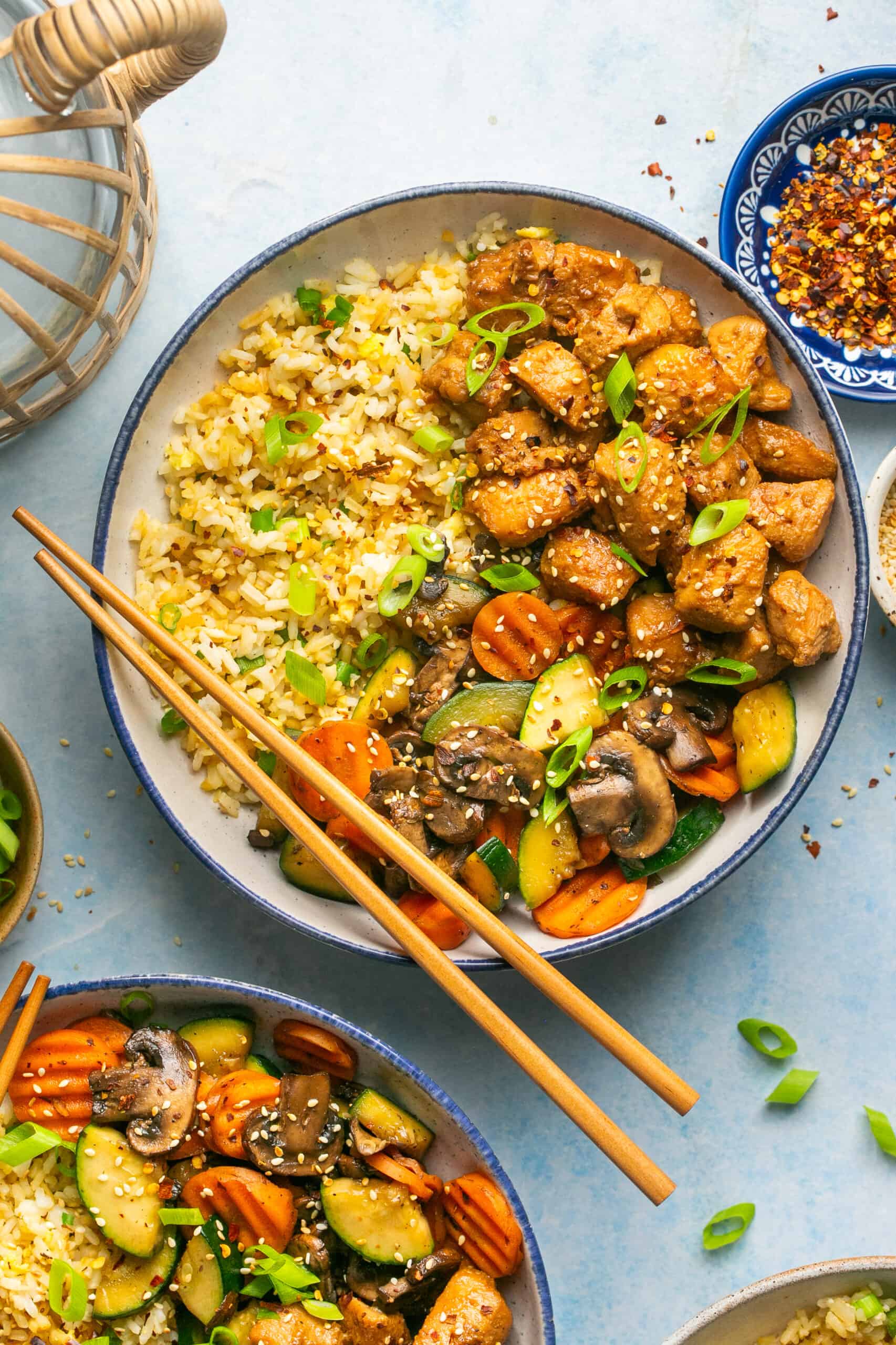 Two bowls of marinated and grilled chicken over fried rice with hibachi style vegetables and chop sticks.