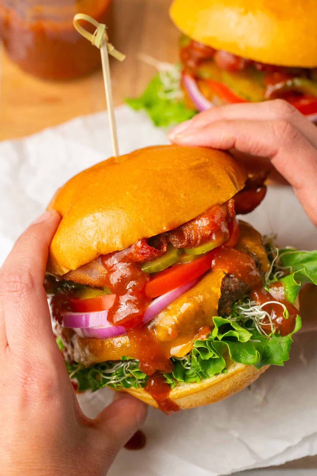 Hands holding a bbq dripping assembled juicy cheeseburger. 