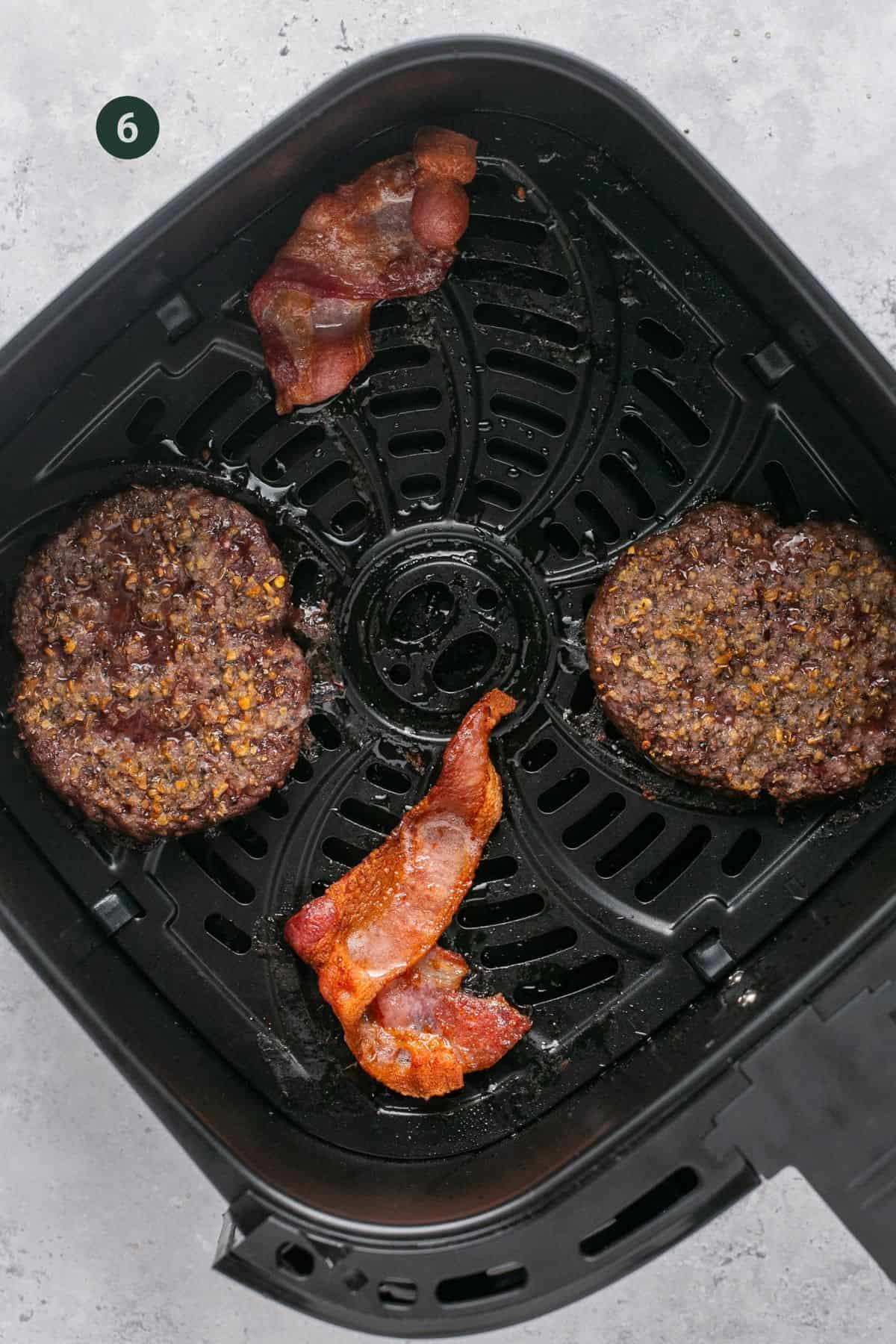 Cooked burgers and bacon in the air fryer basket. 