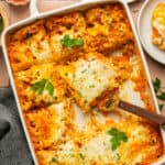Cheesy baked lasagna with a serving utensil pulling out a serving.