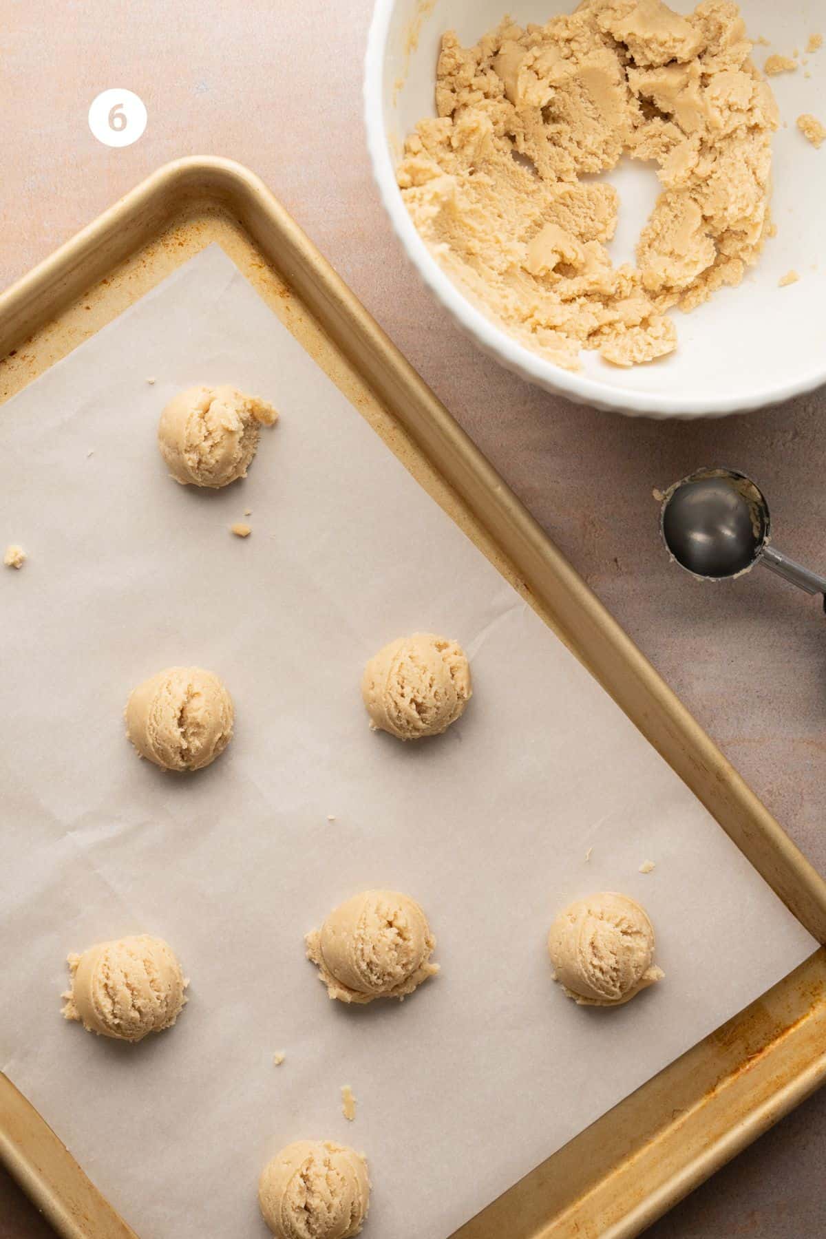 Cookie dough scooped onto a baking sheet to bake with the bowl of dough off to the side. 