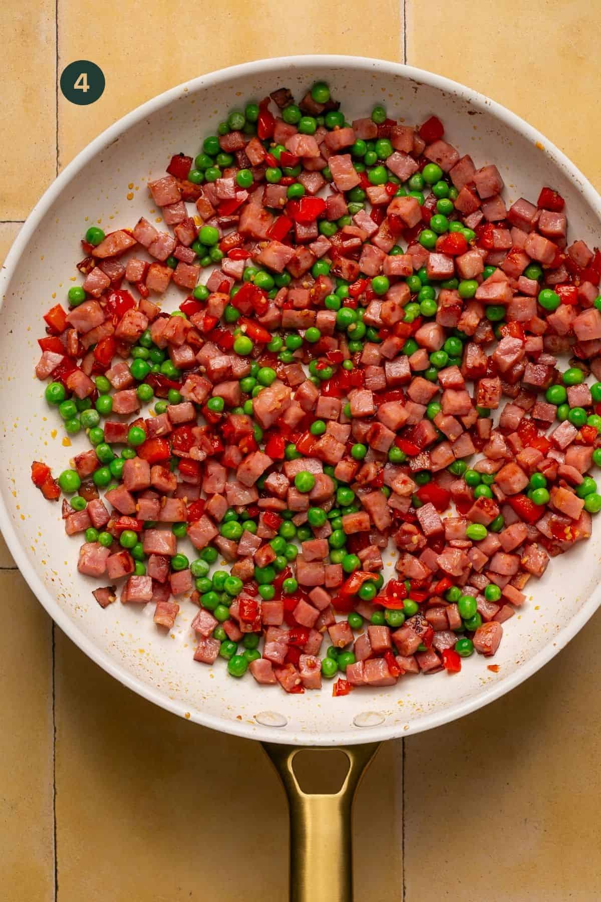 Peas added to ham and bell peppers in a pan.