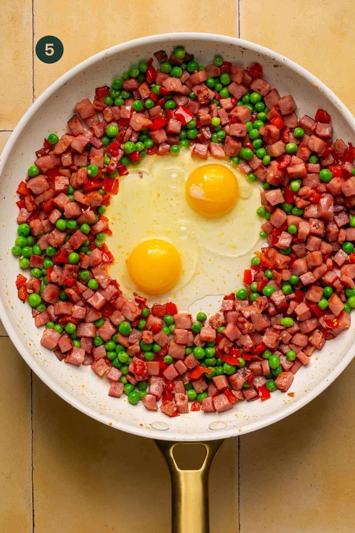 Vegetables and ham pushed to the outer edge of a pan to create a hole in the center with 2 eggs added in the hole.