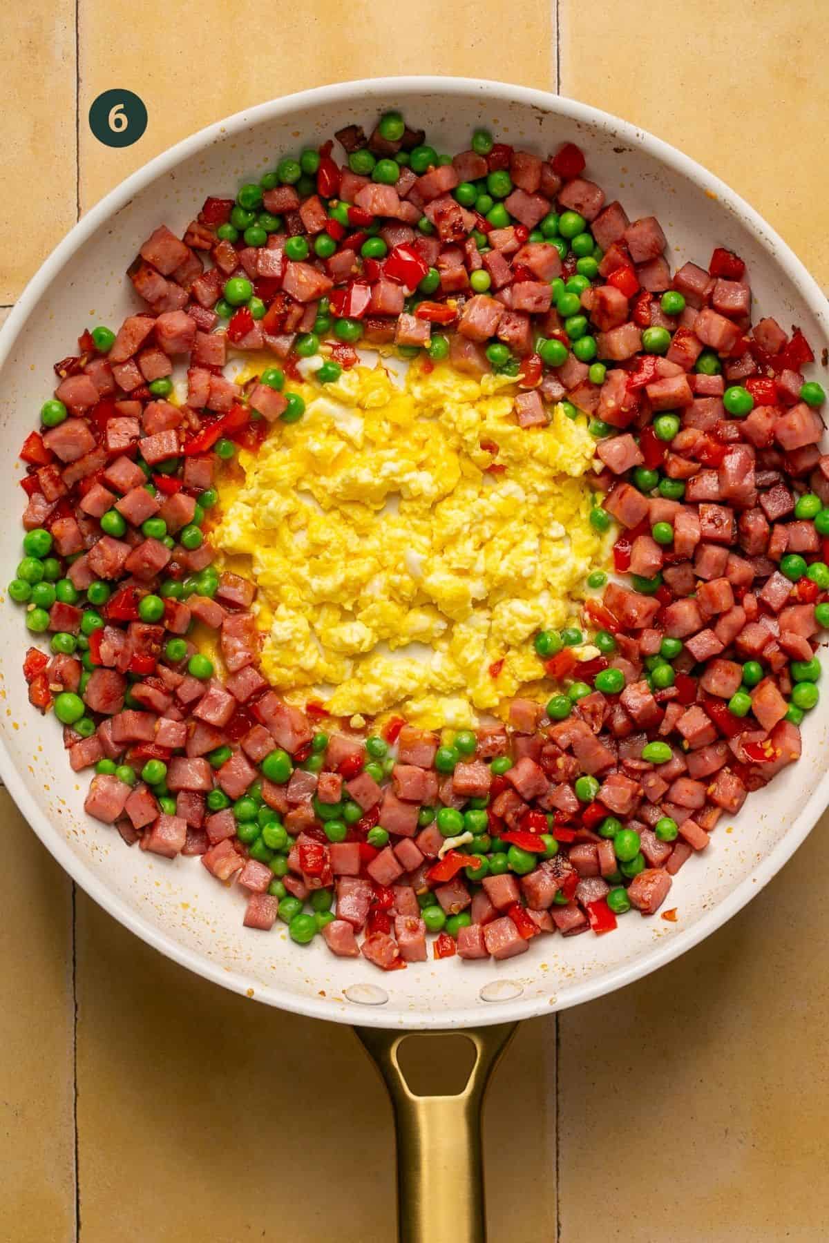 2 eggs scrambled in the center of ham and veggies in a pan.