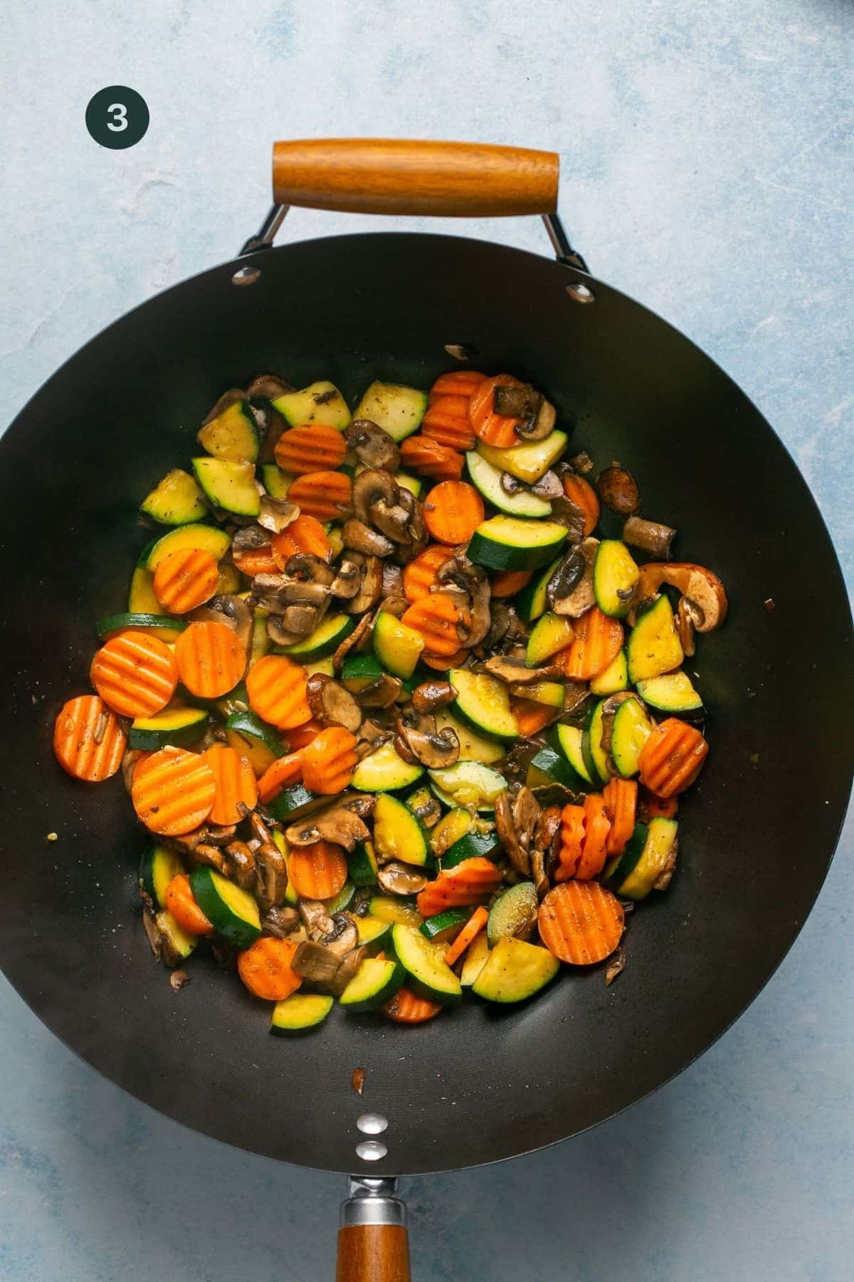 Sauteed carrots, mushrooms and zucchini in a large wok. 