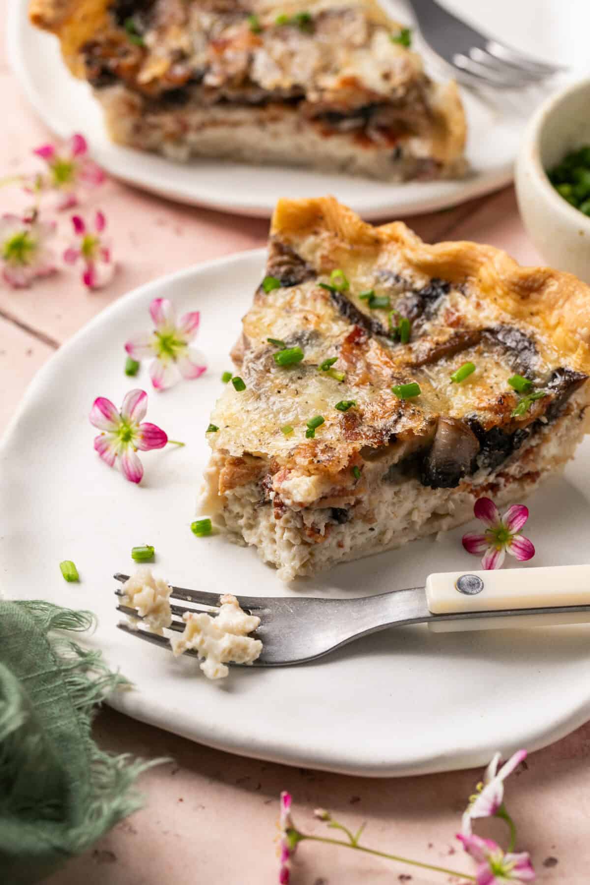 A slice of quiche with a fork plated with flowers. 