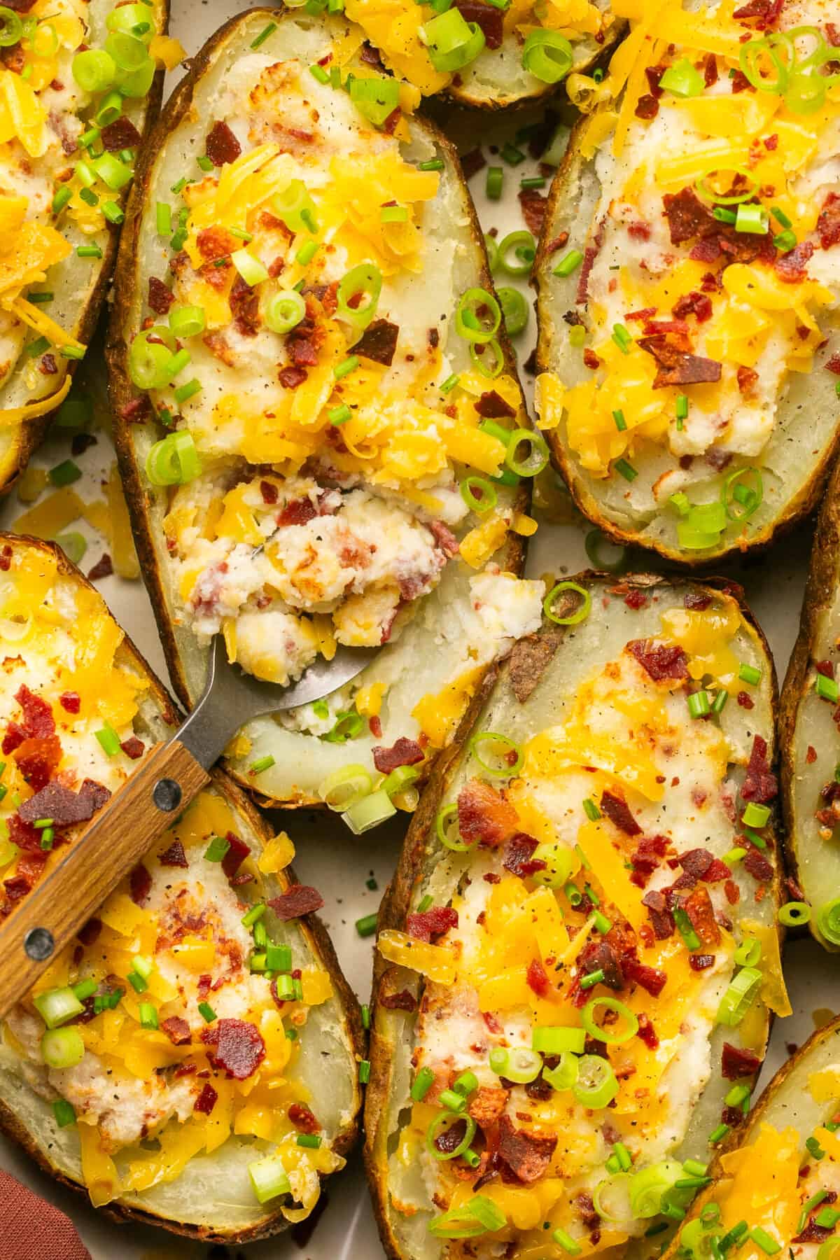 5 twice baked potatoes topped with bacon, cheese and green onions with a spoon scooping some out.