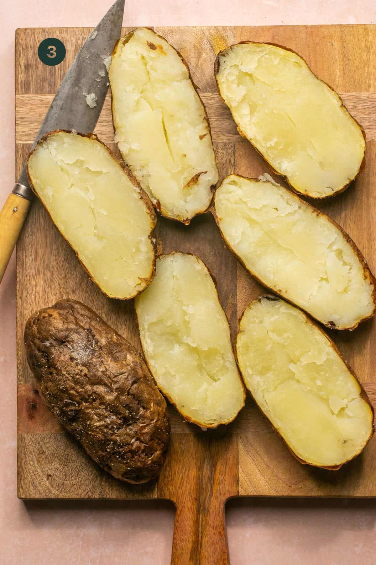 Baked potatoes sliced lengthwise on a wooden cutting board with a knife. 