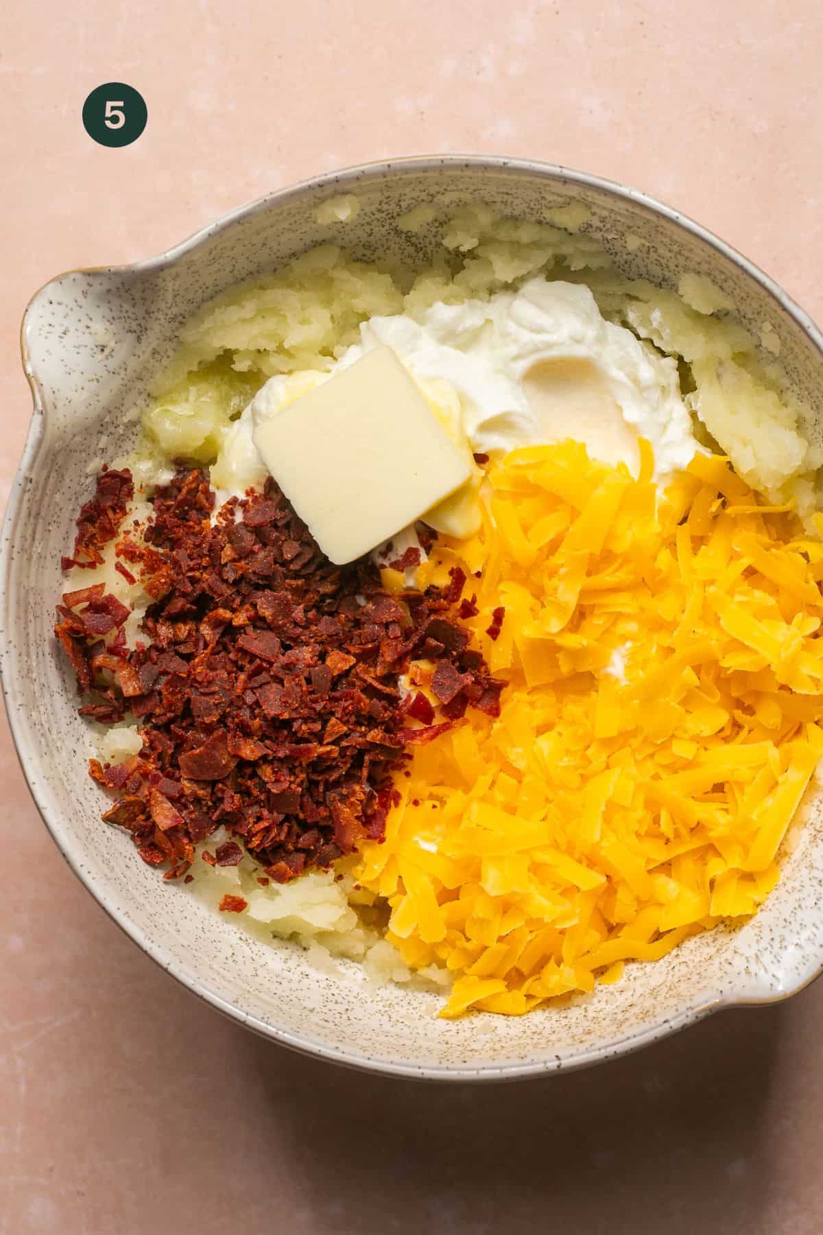 Turkey bacon, shredded cheese and greek yogurt added to mashed potatoes in a bowl. 